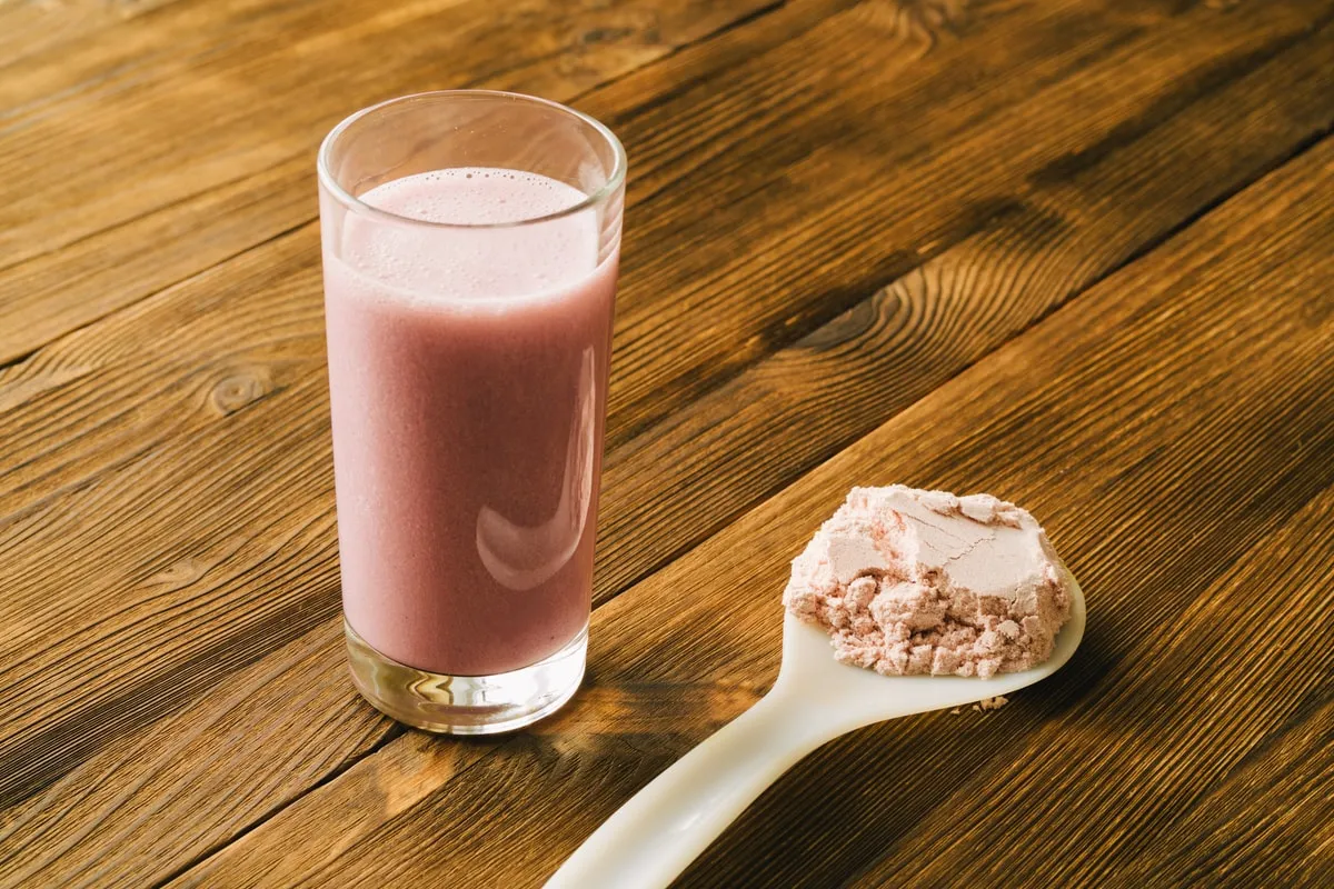 A chocolate shake in a glass beside a wooden scoop of powder