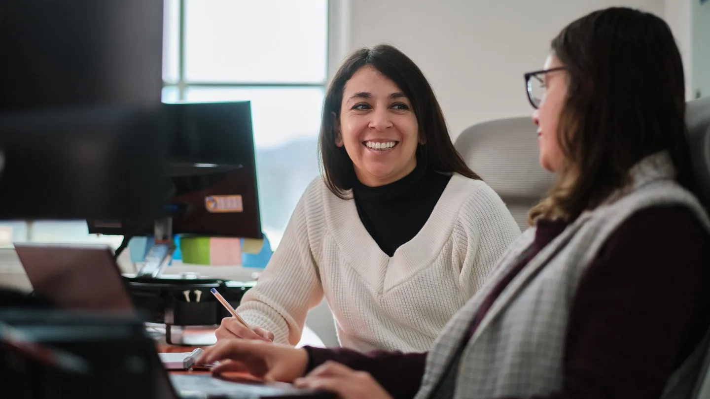Two colleagues talking at a desk in the office