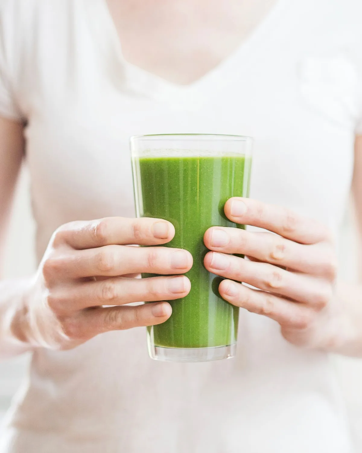 A person holding a glass of green shake with both hands