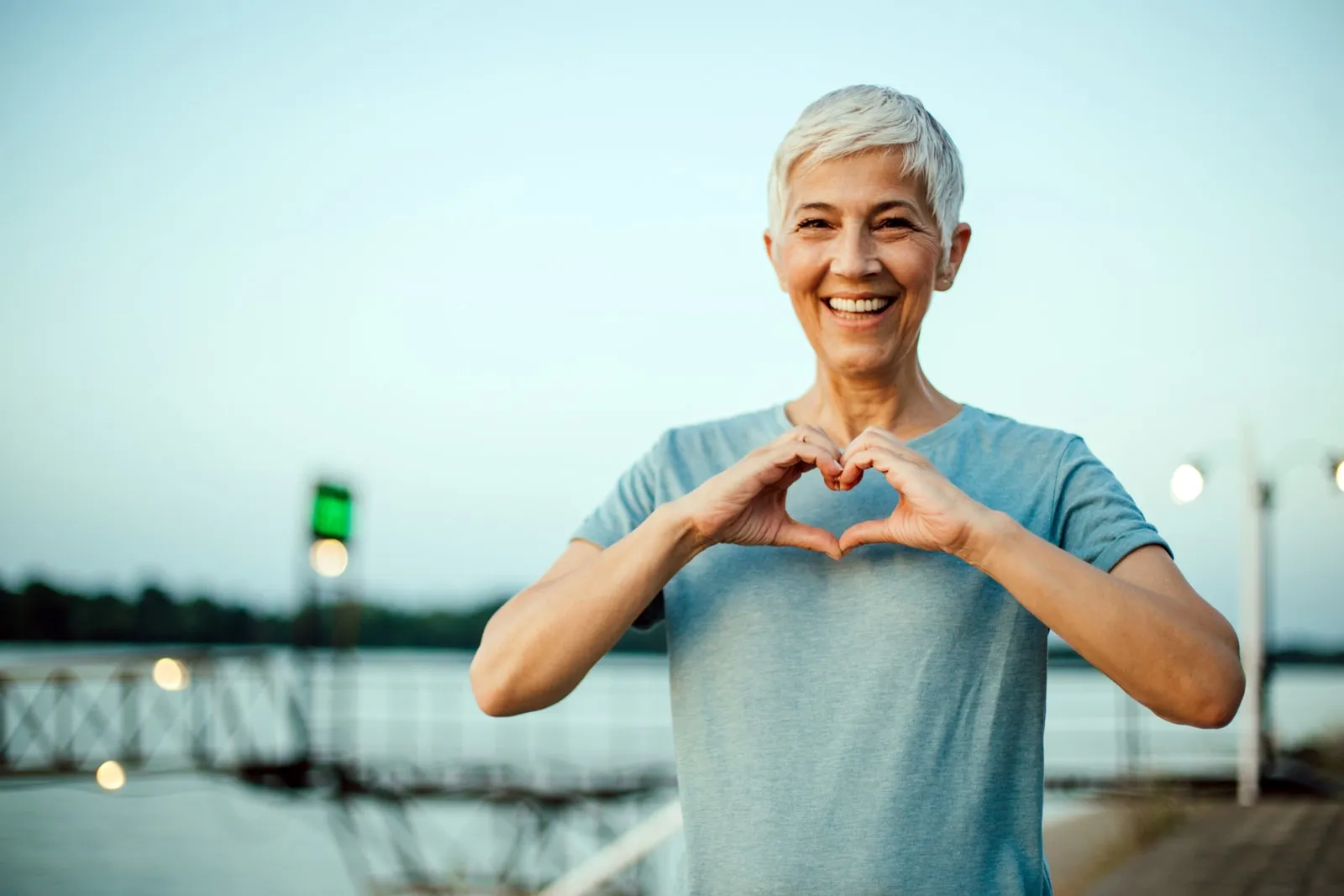 Una mujer forma un corazón con las manos, al aire libre al atardecer
