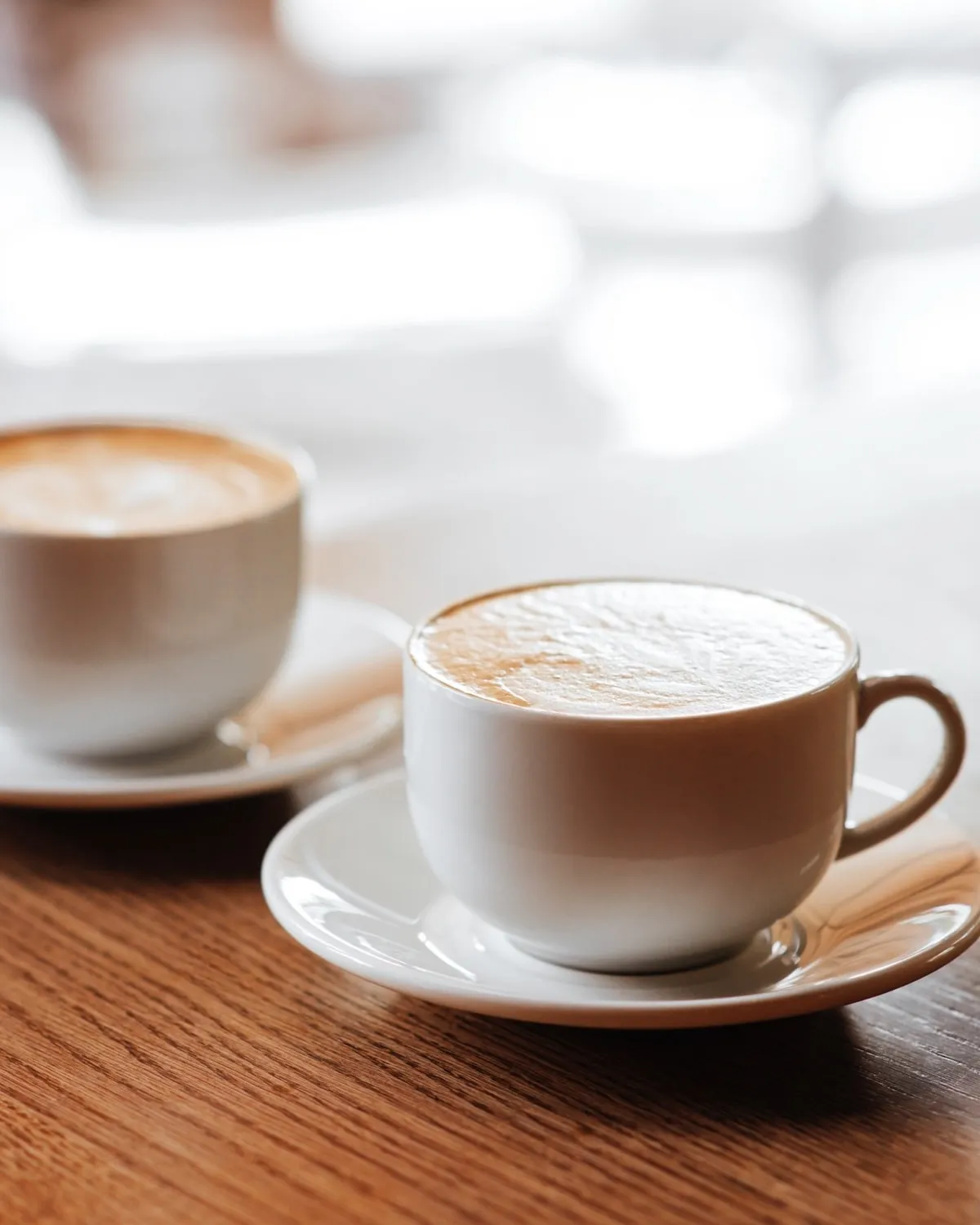 Two cups of latte on saucers on a wooden table