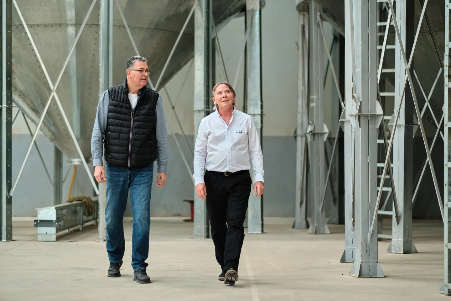 Two people walking between the silos of a chia cleaning facility